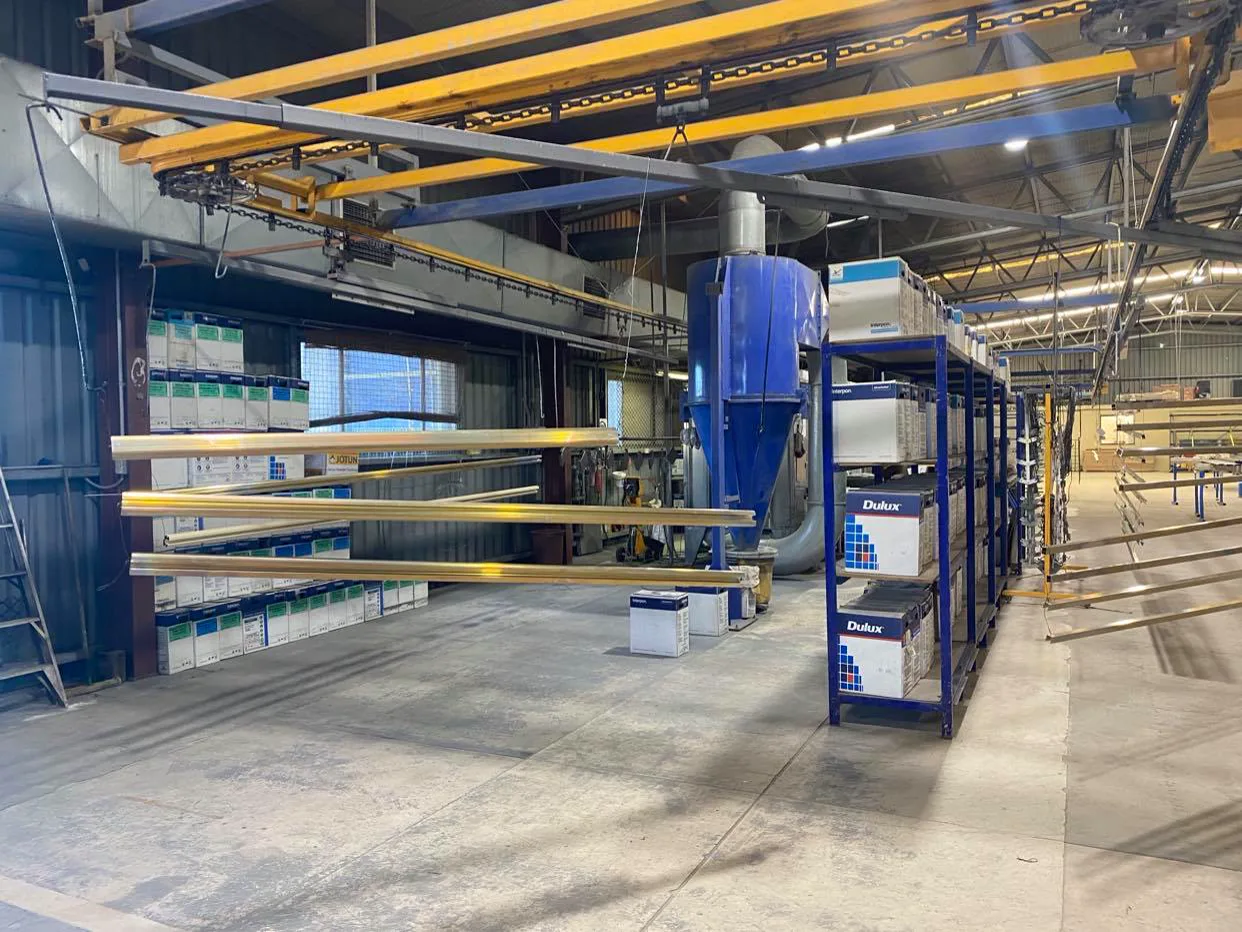 Powder coating line at the OZ Coat workshop with overhead conveyor rails and racked powder stock